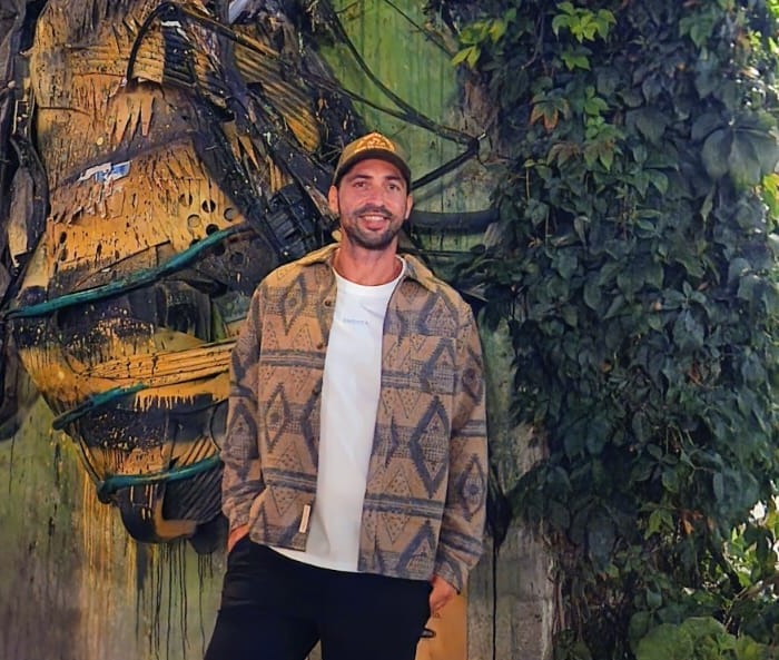 Chris Stellini standing in front of a large recycled-material bee sculpture